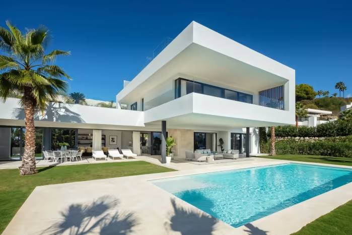 A white villa in Costa del Sol sits in the sunshine next to palm trees and a pool