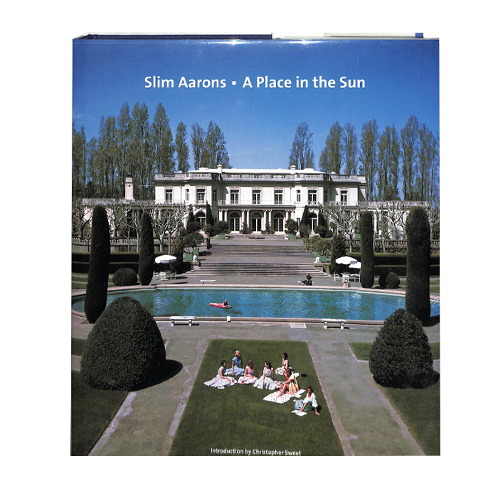 A book cover shows an image of people sitting near a pool in the garden of a large villa