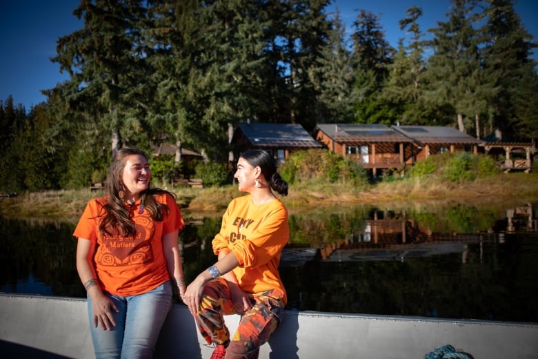 Two women sit on a boat with solar-panelled buildings behind them.