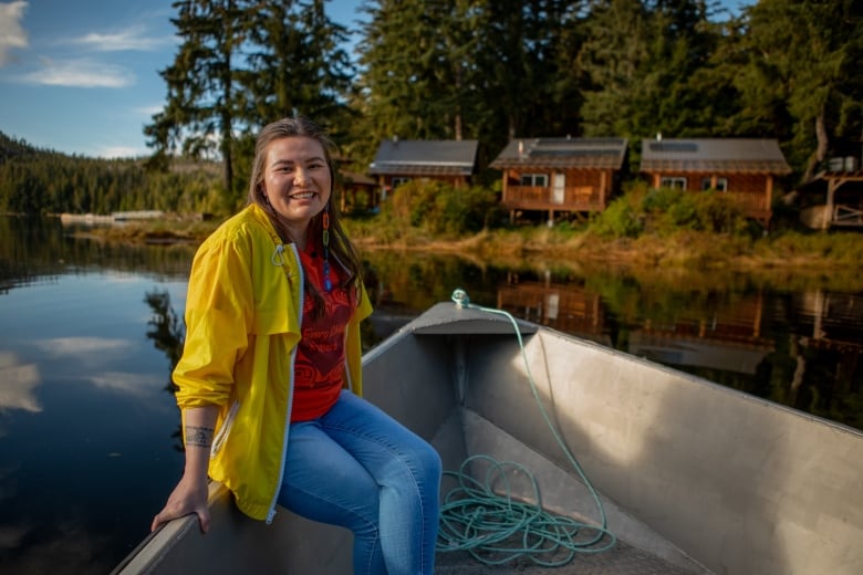 A woman sits on the edge of a boat next to three buildings with solar panels on the roof.