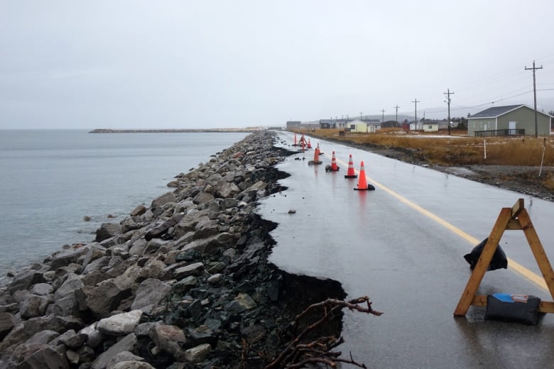 One lane of a coastal road has crumbled into the sea. Pylons separate the cracks from the other lane.