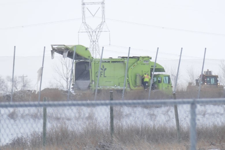 A dump truck is seen behind a chain-link fence on the property of a landfill.