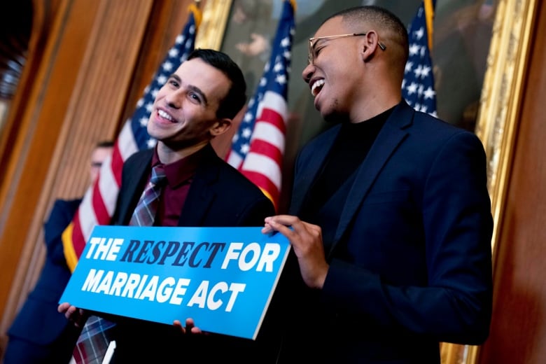 Two individuals, smiling and holding a sign that reads "The Respect for Marriage Act."