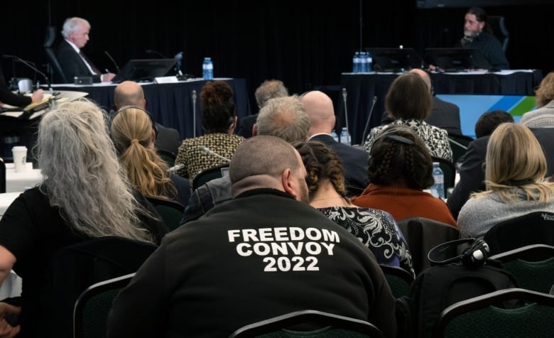 Someone wearing a shirt saying 'FREEDOM CONVOY 2022' watches an inquiry hearing.