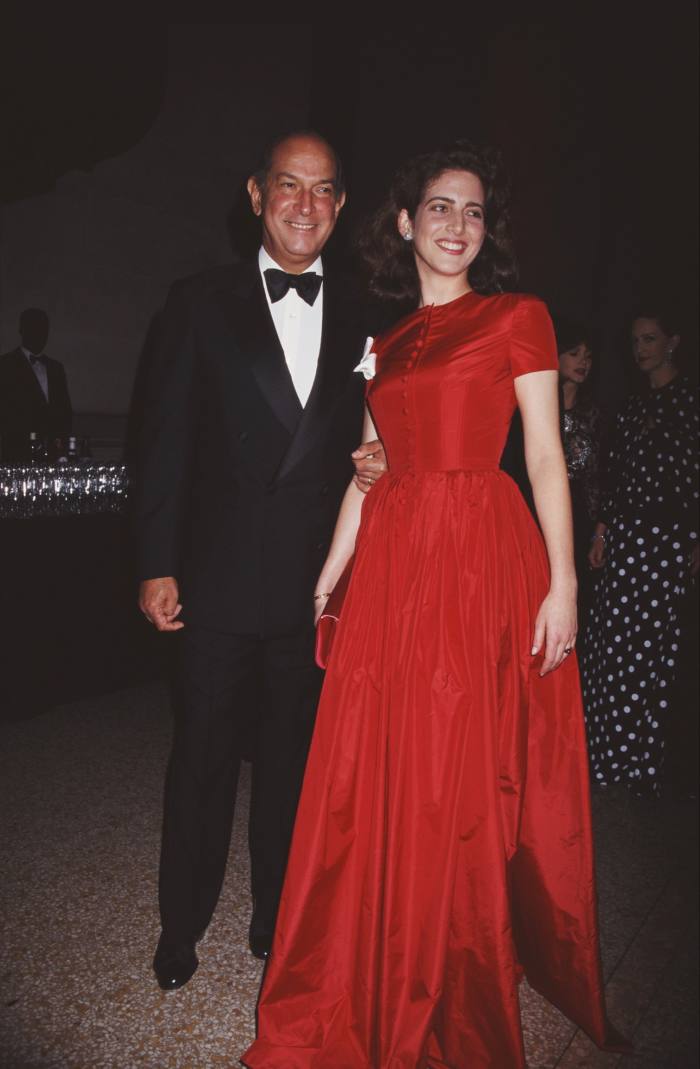 Oscar de la Renta dressed in a black-and-white suit stands with Eliza Bolen in a red dress