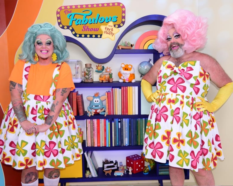 Two drag artists Fluffy Soufflé and Fay Slift stand together in front of a colourful bookshelf for their show -- The Fabulous Show