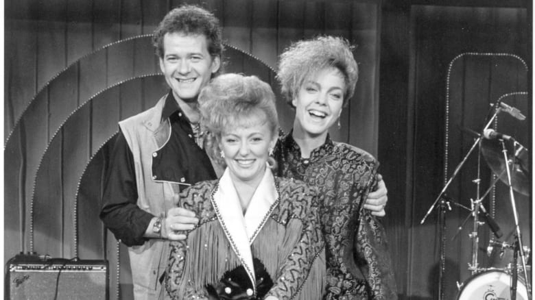 A man and two women are shown posing onstage in a black and white photograph.