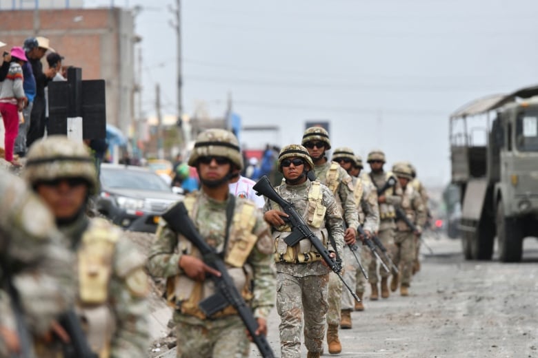 Armed soldiers march along a street. 