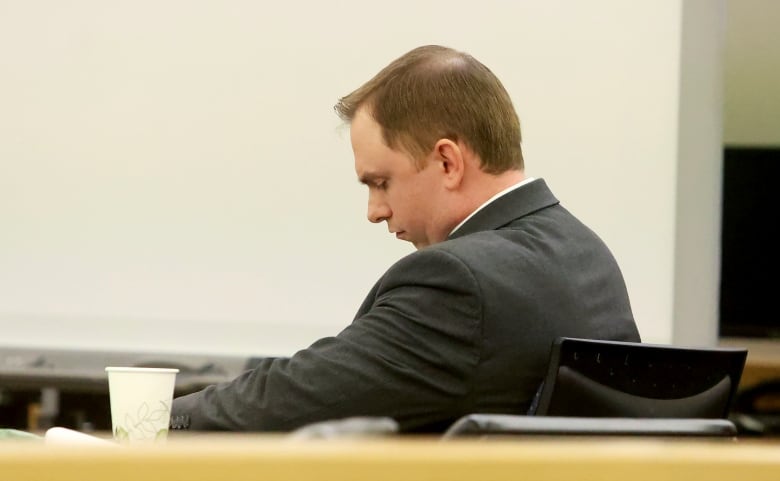 A man sits in a courtroom, his head downcast.