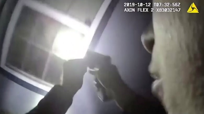 A man points a gun and flashlight into a window, in a still taken from body camera footage. 