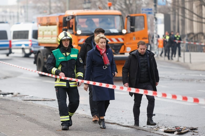 A woman is seen walking between two men, one a first responder who is wearing a helmet.