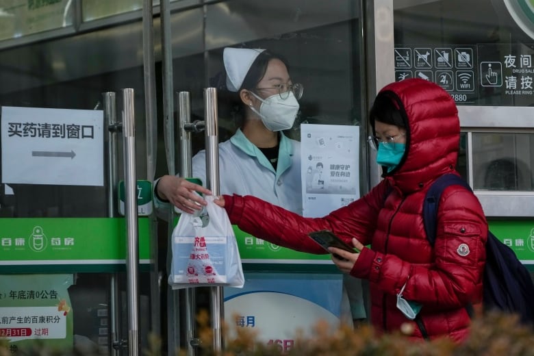 A woman in a red coat and face mask takes a plastic bag from another woman.