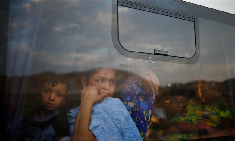 A woman sits on a bus with a child in her lap, looking out the window.