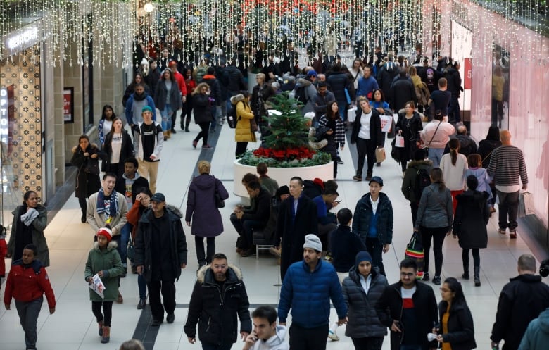 Crowds of people holding shopping bags walk through a mall.