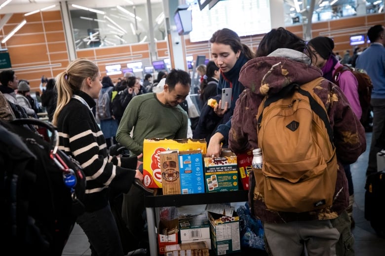 Travellers gather around a black cart piled with free snacks at Vancouver International Airport.