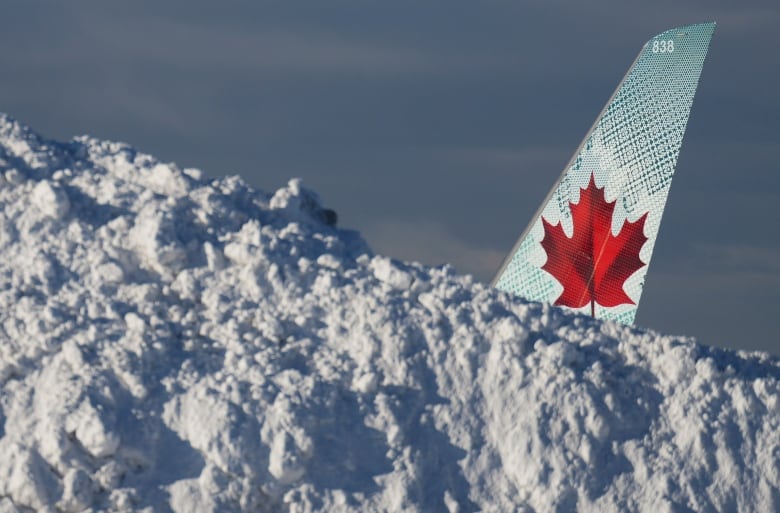 A tail with Air Canada's red Maple Leaf livery peeks out from behind snow that takes up most of the frame. None of the rest of the plane is visible.