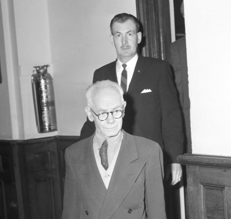 A man enters leaves the courtroom, shadowed by another man behind him.