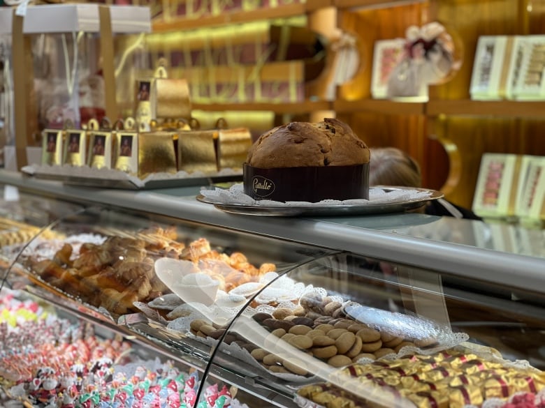 A round panettone Italian sweet bread sits on a glass display case filled with cookies, chocolates and treats.