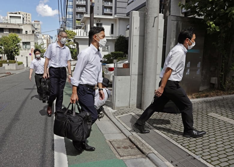 Law enforcement officers in Japan enter a building  with duffel bags.