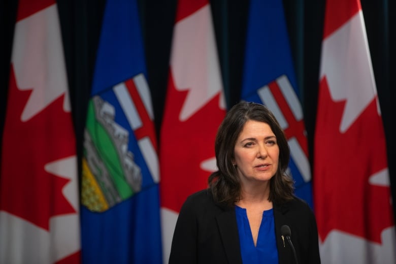 Alverta Premier Danielle Smith addresses media at a podium with Canadian and Alberta flags behind her.