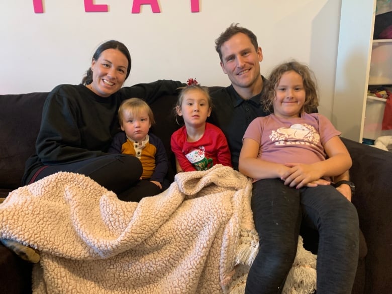 Michelle and Ty Hughes pictured on a couch at home with their three kids.