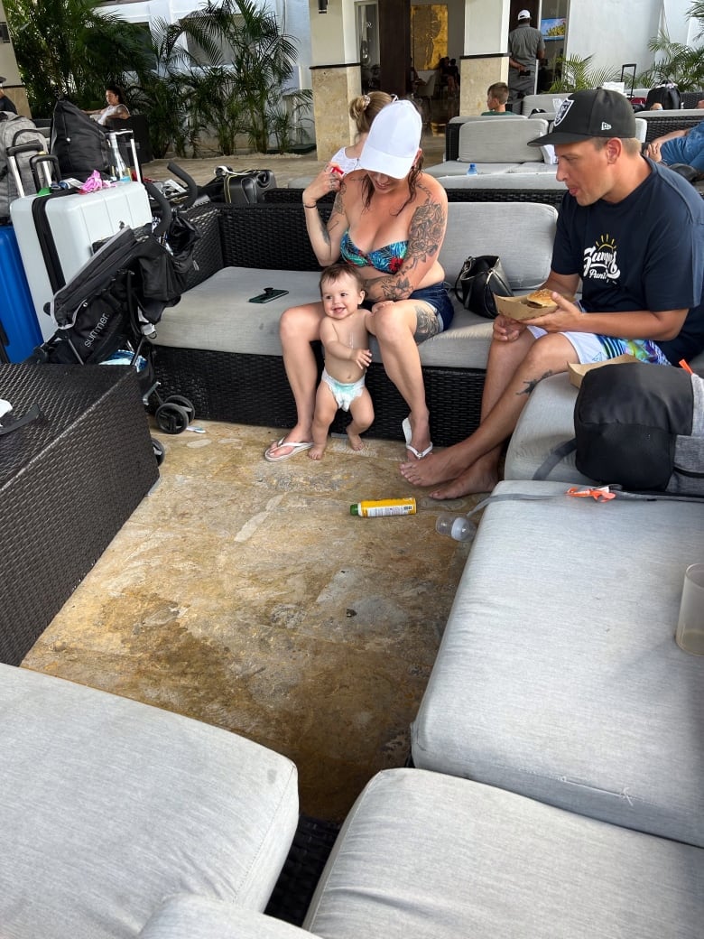 A man and woman play with a baby in diapers and luggage is also seen.