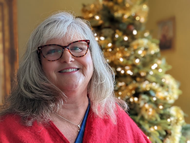 A smiling woman stands in front of a glowing Christmas tree.