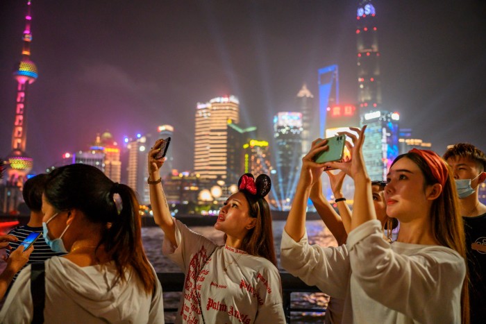 Women take photos along the Huangpu River against the Shanghai skyline