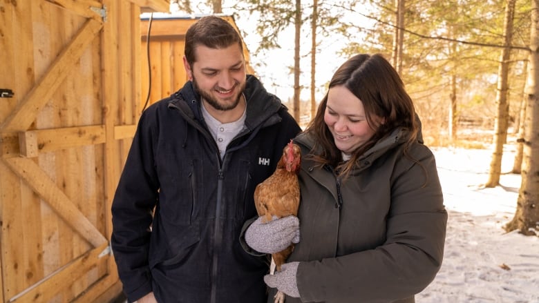 A man and woman hold a chicken and smile looking at it.