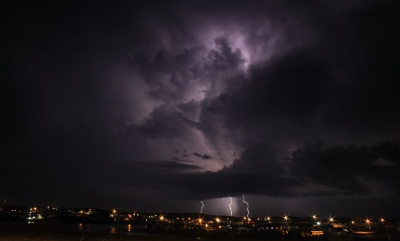 Three strike of lightning can be seen at night above a city of lights.