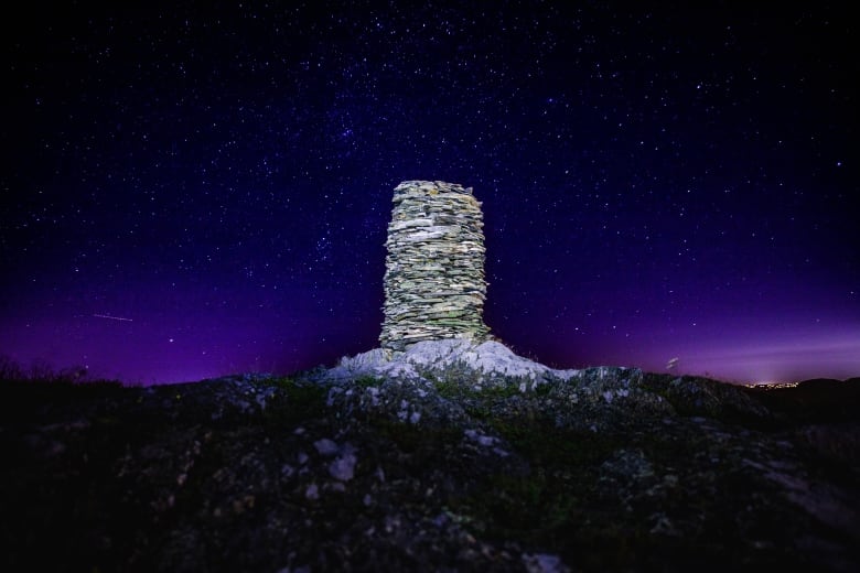 A strange rock structure, a cylinder shape comprised of thousands of small stones, is illuminated against a night sky filled with stars. 