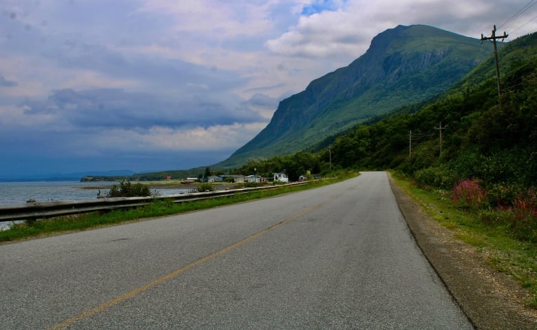 A two-lane road into the town of York Harbour, with tree-covered hills looming in the cloudy sky above it all.