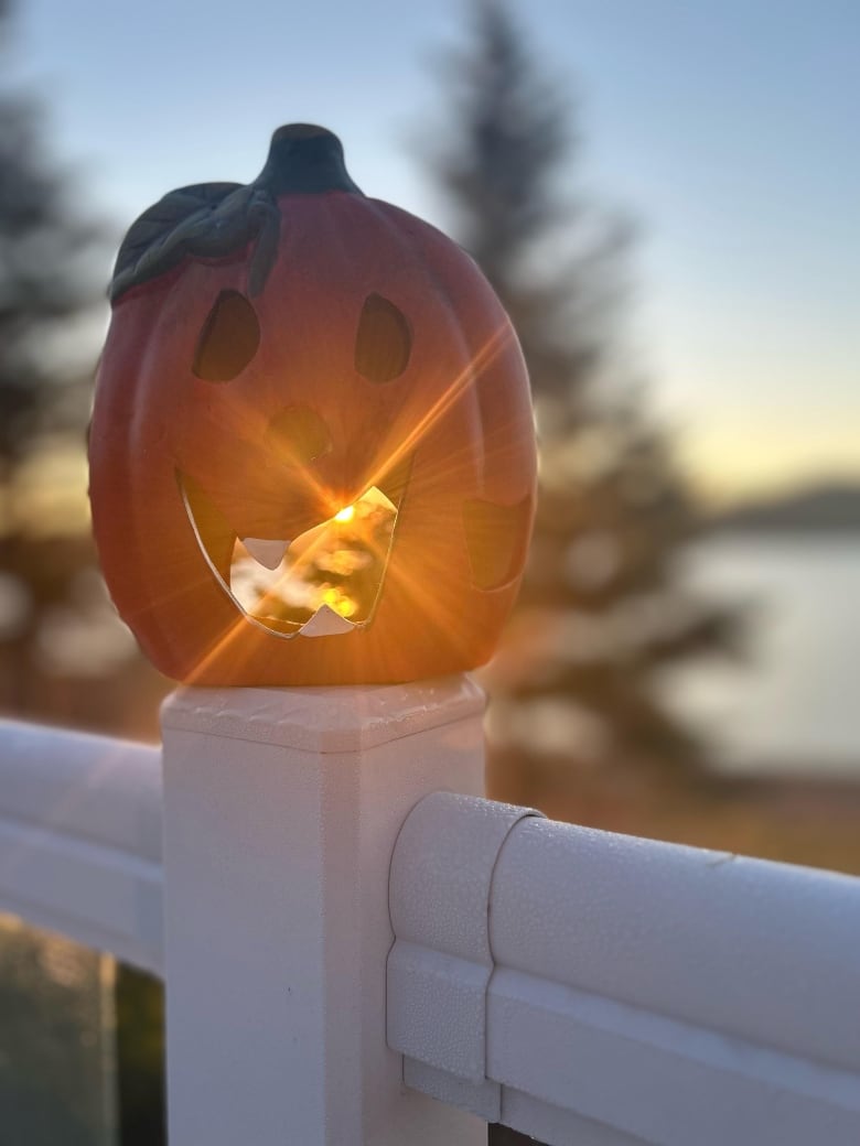 The sun shines through the mouth of a hollow jack-o-lantern placed on the post of a porch staircase.