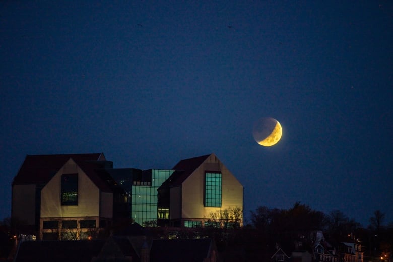 The shadow of the Earth cuts the moon in half, hovering in space over the Rooms museum in St. John's.