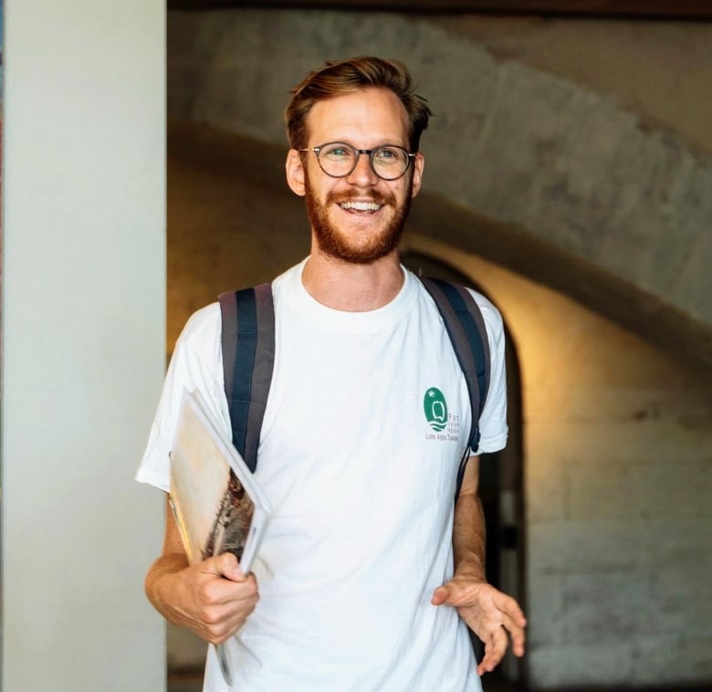 Man in white shirt wearing a backpack and big smile