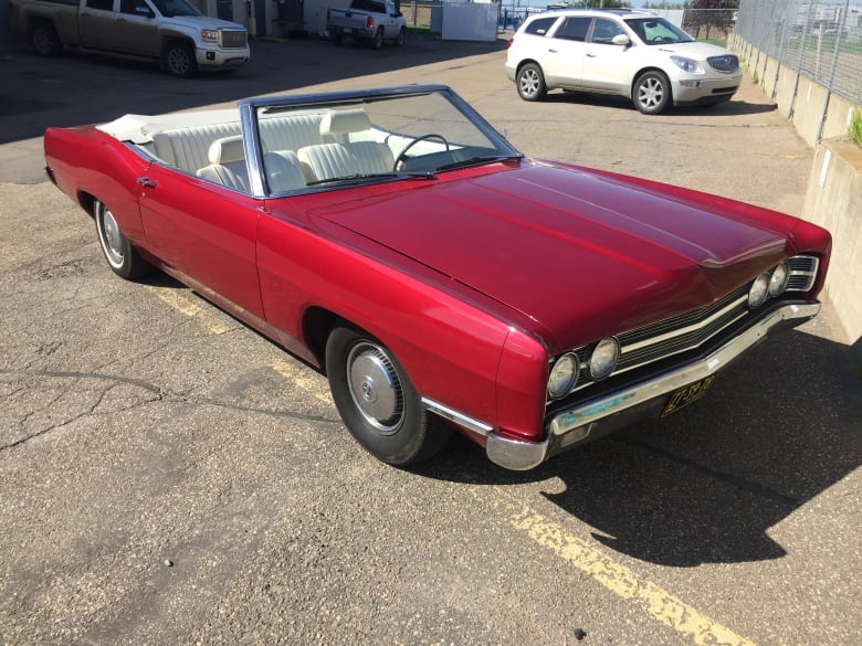 An old red convertible car parked outside on a sunny day. 