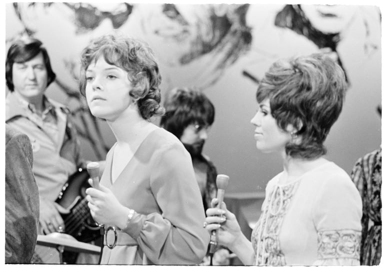 Two women singers are seen in in the foreground in front of musicians in a black and white photograph.