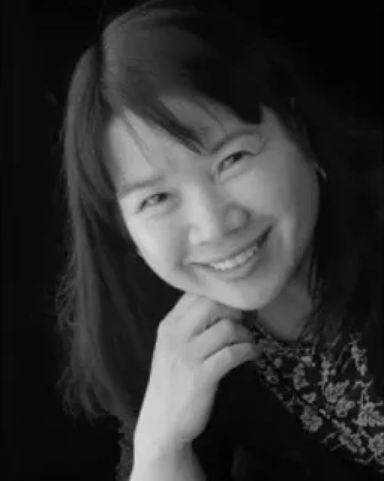 A black and white headshot shows an East Asian woman with mid-length hair posing with her head tilted to the side and her hand held under her chin.