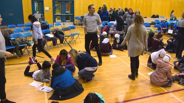 Students play together in groups on the wooden floor of an elementary school gymnasium.