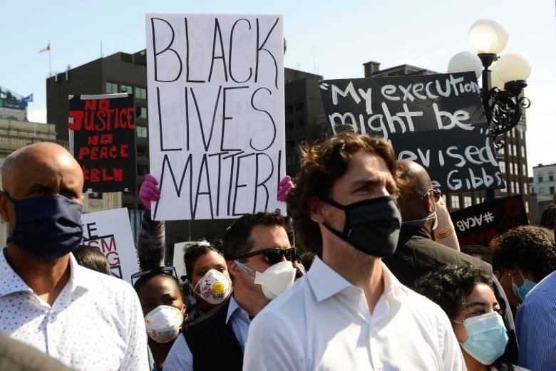 A protester holds up a Black Lives Matter sign behind Prime Minister Justin Trudeau as  people take part in an anti-racism protest on Parliament Hill during the COVID-19 pandemic in Ottawa on Friday, June 5, 2020. 