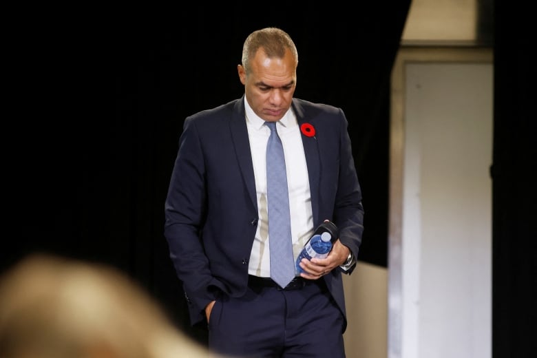 A man in a suit carries a water bottle and glasses case.