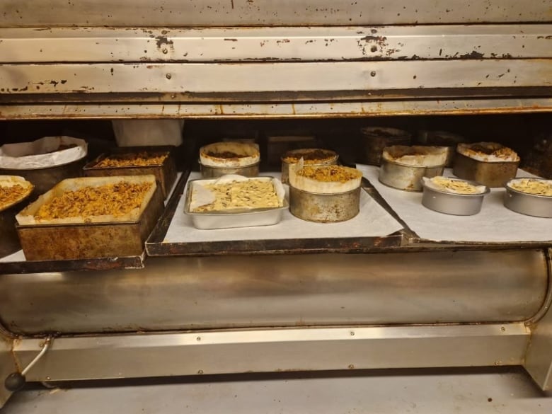 A large oven with the door open, revealing several baking sheets loaded with pans full of cake. 