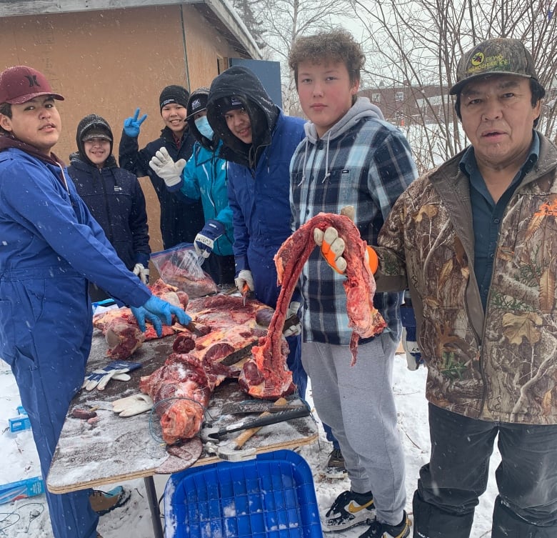 Students and community members prepare meat together in Behchokǫ̀.