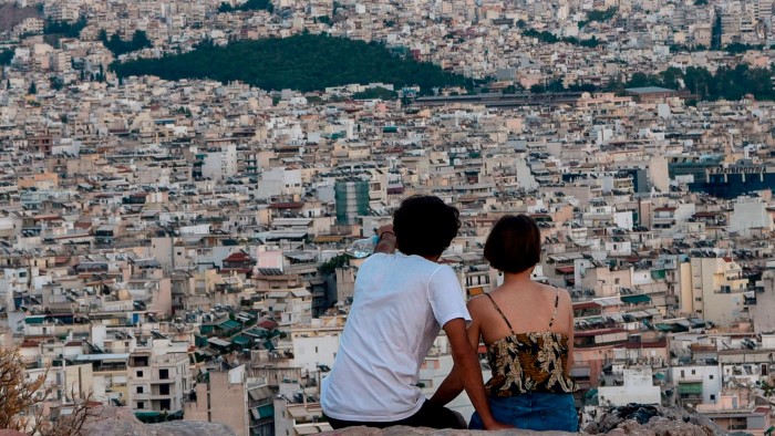 A couple sits on a hill looking at the buildings of Athens 