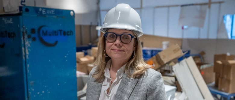 A woman in a business suit and a hardhat stands in a room under construction.