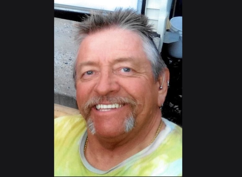 A man with grey hair in a yellow shirt smiles toward the camera.