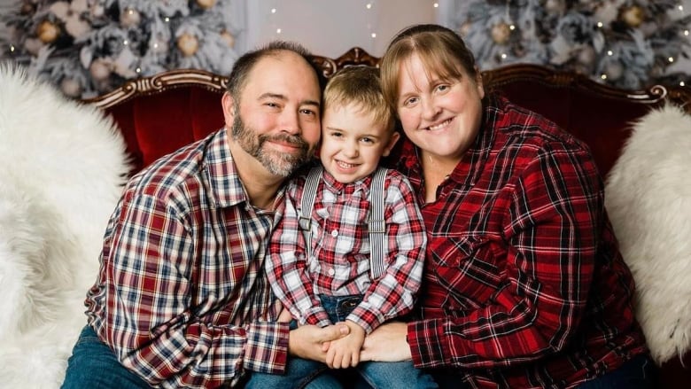 Three people, all wearing red plaid, hug and smile. The person in the middle is a young child.