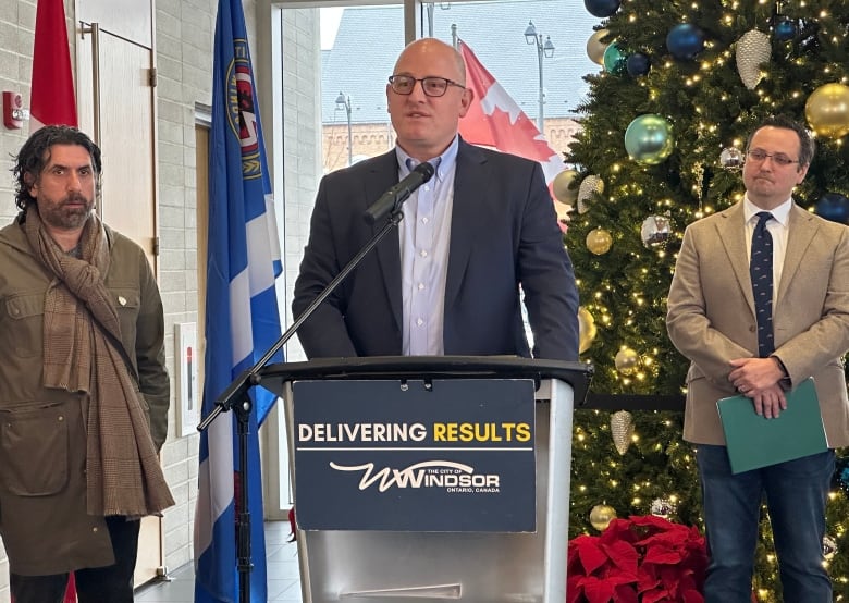 Three men stand at a podium at City Hall. 