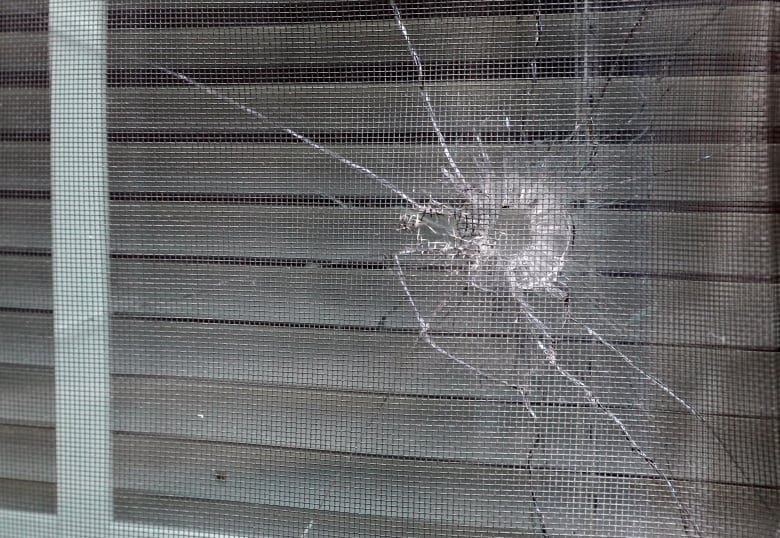 A bullet hole is seen in the rear window of a house.