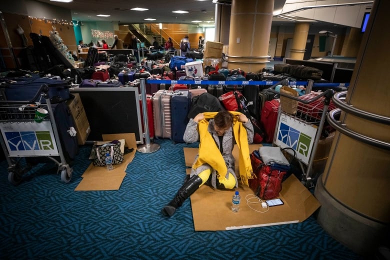 A woman with glasses seated on the floor adjusts her yellow scarf.